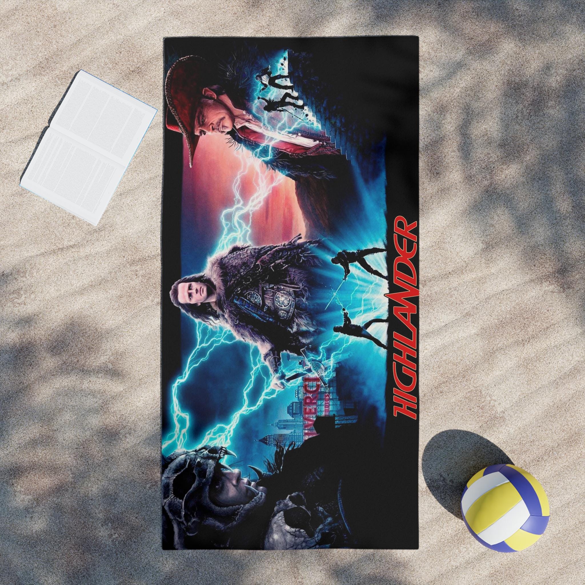 Towel with 'Highlander' movie poster design on a sandy surface