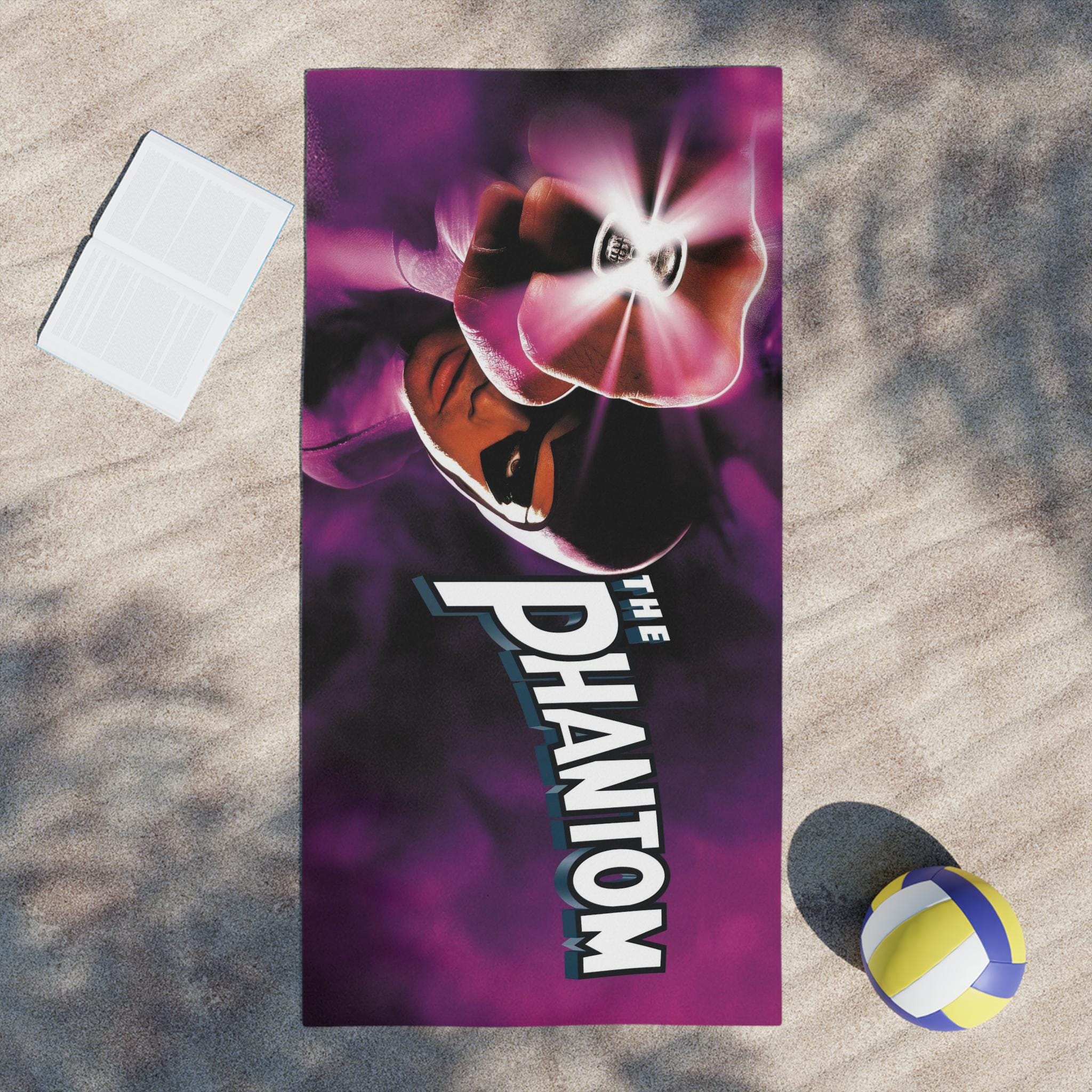 Towel with 'The Phantom' design on a sandy surface with a volleyball.